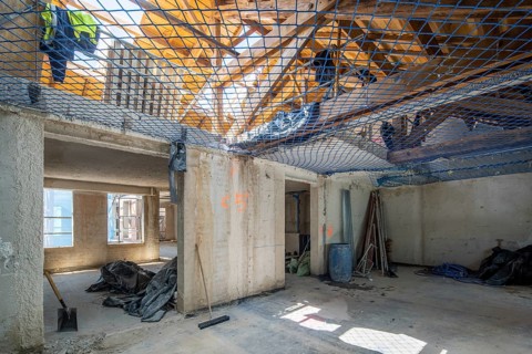 Interior view of a building under construction. Tools, safety netting, and equipment are visible,
