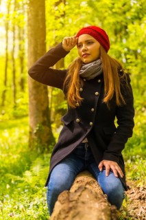 Woman with a black jacket and a red hat enjoying in an autumn park, sitting on a tree smiling at