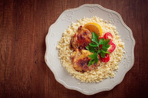 Couscous is served on a plate with pieces of chicken on top. Lemon slices and parsley decorate the
