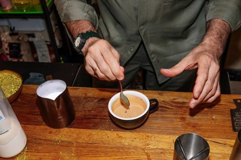 A barista skillfully stirs a freshly brewed specialty coffee in a cozy coffee shop setting. The