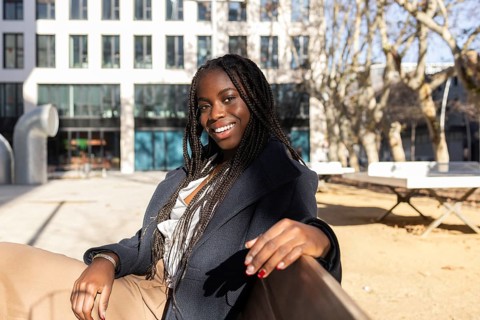 A smiling young African American businesswoman with braids relaxes outdoors during a work break