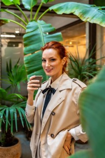 Vertical portrait of a chic woman standing drinking coffee at the entrance of the office