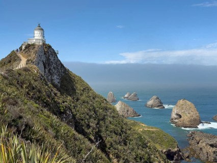 Nugget Point Lighthouse with Nugget Rocks in front of a blue sky, South Island, New Zealand,