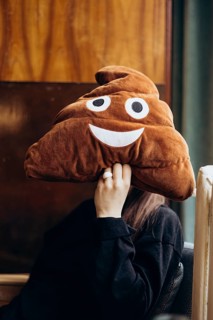 Cropped unrecognizable young woman holding a large plush poop emoji toy over her face in a cafe,