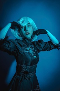 Portrait of cosplay woman in black costume and a white wig in studio with blue led light