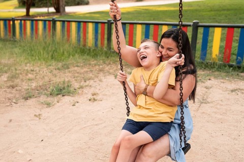 A loving mother and her disabled son with cerebral palsy share a joyful moment on a swing in a