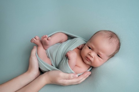 A serene image of a newborn baby gently cradled in an adult's hands. The baby is wrapped in soft,
