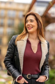 Young female journalist smiling and looking away while posing with hands in pockets in a blurred