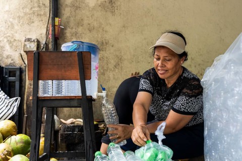A woman fills bottles with fresh coconut water. She smiles while working in a casual outdoor