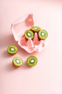Top view of fresh kiwi slices neatly placed inside a pink egg carton on a soft pink background,
