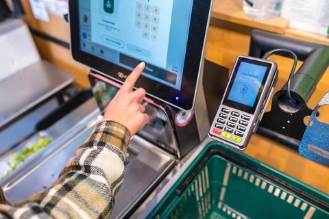 Person using self checkout and payment terminal in a san francisco grocery store, tapping card on