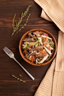 Meat salad with beef and vegetables in wooden bowl on brown wooden background and linen textile.