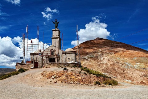 A building with a statue on a mountain surrounded by antennas under a blue sky with clouds, The