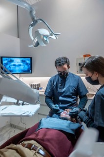 Dentist and assistant wearing masks and gloves performing a dental checkup on a patient in a modern