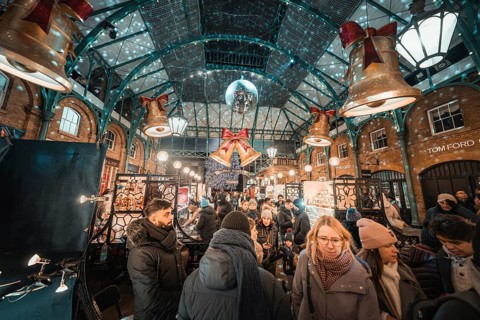 Crowd at a busy Christmas market surrounded by decorative bells and lights, AppleMarket, London,