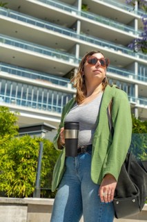 Businesswoman wearing sunglasses holding reusable coffee cup standing near modern building