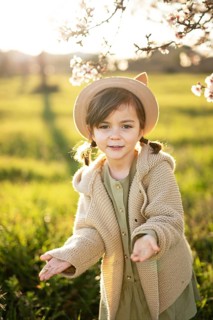 A young girl in a beige hat and sweater joyfully explores a sunlit field surrounded by almond