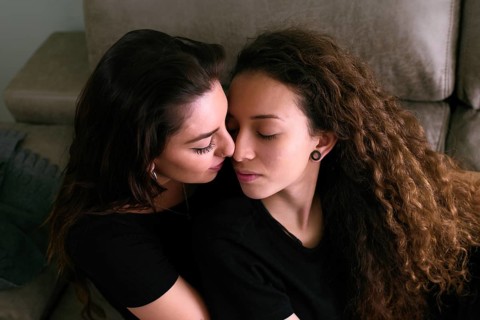 Tender scene of a female gay couple sharing a loving embrace in their cozy living room, one kisses