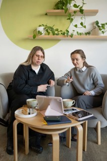 Two women are sitting in a cozy cafe, engaging in a lively discussion over cups of coffee and using