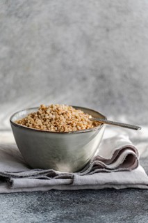 A rustic bowl filled with chopped hazelnuts, resting on a gray textured cloth with a vintage spoon