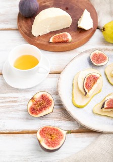Summer appetizer with pear, cottage cheese, figs and honey on a white wooden background and linen