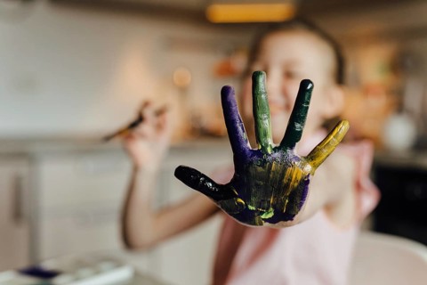 A joyful child showcases a hand covered in vibrant paint, expressing creativity and fun in an