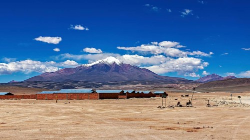 Lonely desert landscape with snow-covered mountain and blue sky in the background, lined with