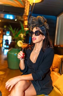Vertical photo of a cool woman in sunglasses drinking a cocktail in a luxury night bar