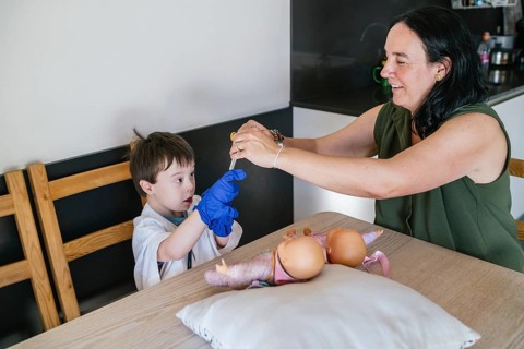 A mother and her son, who has Down syndrome, engage in imaginative play at the kitchen table. The