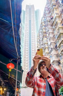 A middle-aged man uses his yellow smartphone to take photos of the bustling street scene in Hong