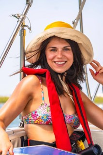 Happy tourist wearing a life jacket, sun hat, and bikini top, enjoying a summer boat trip along the