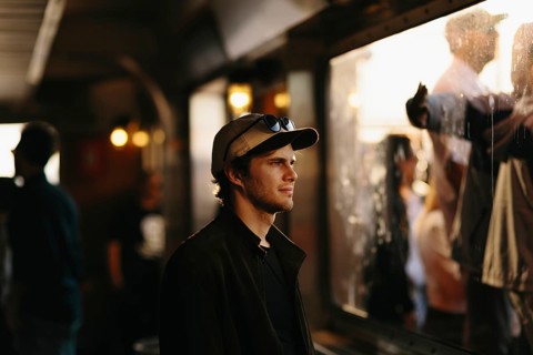 A young man in a casual cap gazes through a window, capturing a thoughtful moment amid the lively