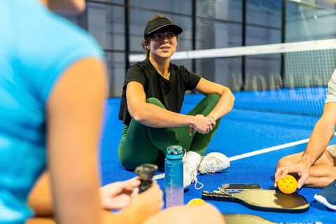 Young female athlete wearing a visor and athletic wear, sitting cross legged on a bright blue