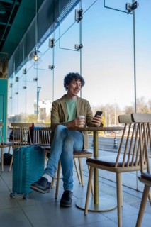 A relaxed man with a suitcase enjoys a coffee while using a smartphone in a modern cafe, capturing