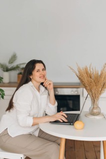 A nutritionist sits in a modern kitchen, smiling while working on a laptop. An lemon and decorative