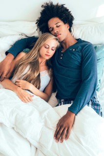 A serene couple is peacefully sleeping and embracing in a cozy bed. They radiate warmth and