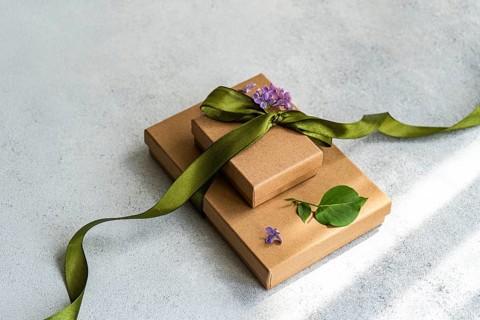 Two brown gift boxes topped with a green ribbon and lilac flowers. A green leaf adds a natural