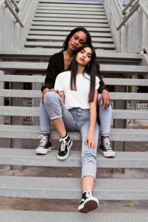 Two stylish friends relax on urban stairs, showcasing casual fashion. Jeans, t shirts, and sneakers