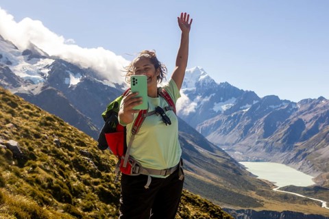 A woman is hiking on Mount Cook, New Zealand, during autumn. She joyfully takes a selfie with
