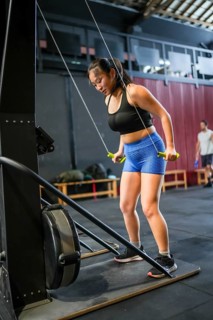 Vertical photo full length of an asian woman working out in a gym with a pulldown lat machine