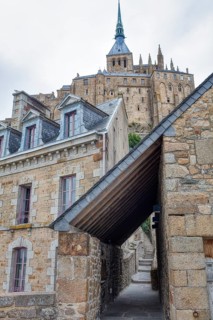Historic stone buildings lining a narrow street with a church in the background, Le