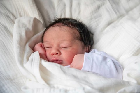 A newborn baby peacefully sleeps wrapped in a soft white blanket, showcasing the tender moments of