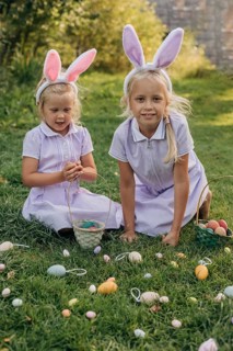 Two children wearing bunny ears participate in a joyful Easter egg hunt on a sunny day. They gather