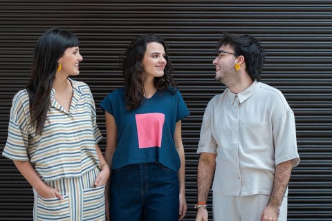 A group of three friends, two women and a man, are enjoying a light-hearted conversation outdoors