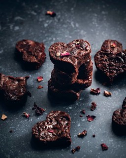 A stack of heart-shaped chocolate treats intertwined with delicate rose petals, creating an elegant
