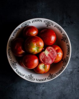 A top down view of fresh, vibrant tomatoes in a decorative ceramic bowl against a dark background.