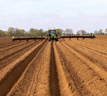 John Deere 6R tractor with wide-boom conveyor system planting platform for potatoes, Shottisham,