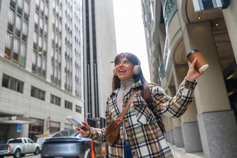 Young woman confidently walking along a city street, listening to music through headphones, holding