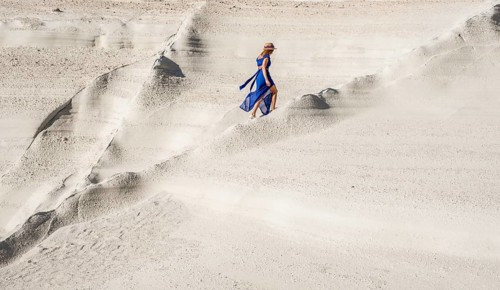Back view of an unrecognizable woman in a flowing blue dress and hat walking on the white moon-like