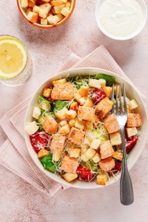 Caesar salad with salmon, with croutons and dressing, in a salad bowl, on a pink table
